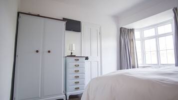 Een slaapkamer met een groot bed, een kledingkast, een dressoir, een televisie en een raam met gordijnen.