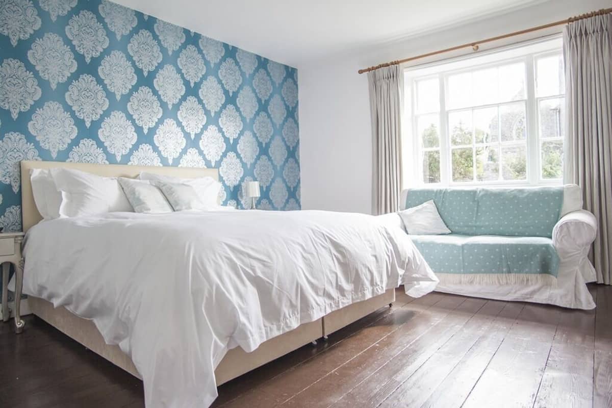 A bedroom with a large bed, a sofa, a window with curtains, and a patterned wall.