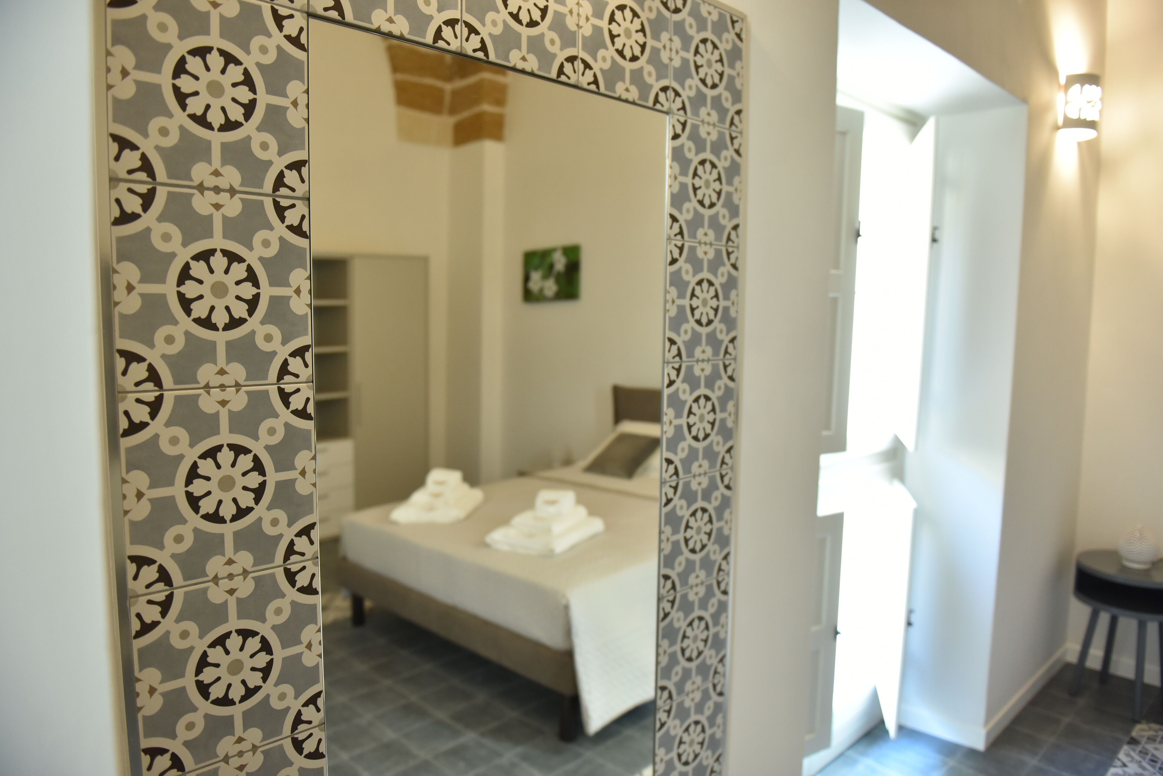 Um quarto com uma cama, um espelho e uma porta que dá para outro cômodo.