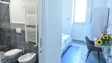 A bathroom with a shower, toilet, bidet, and a towel rack.