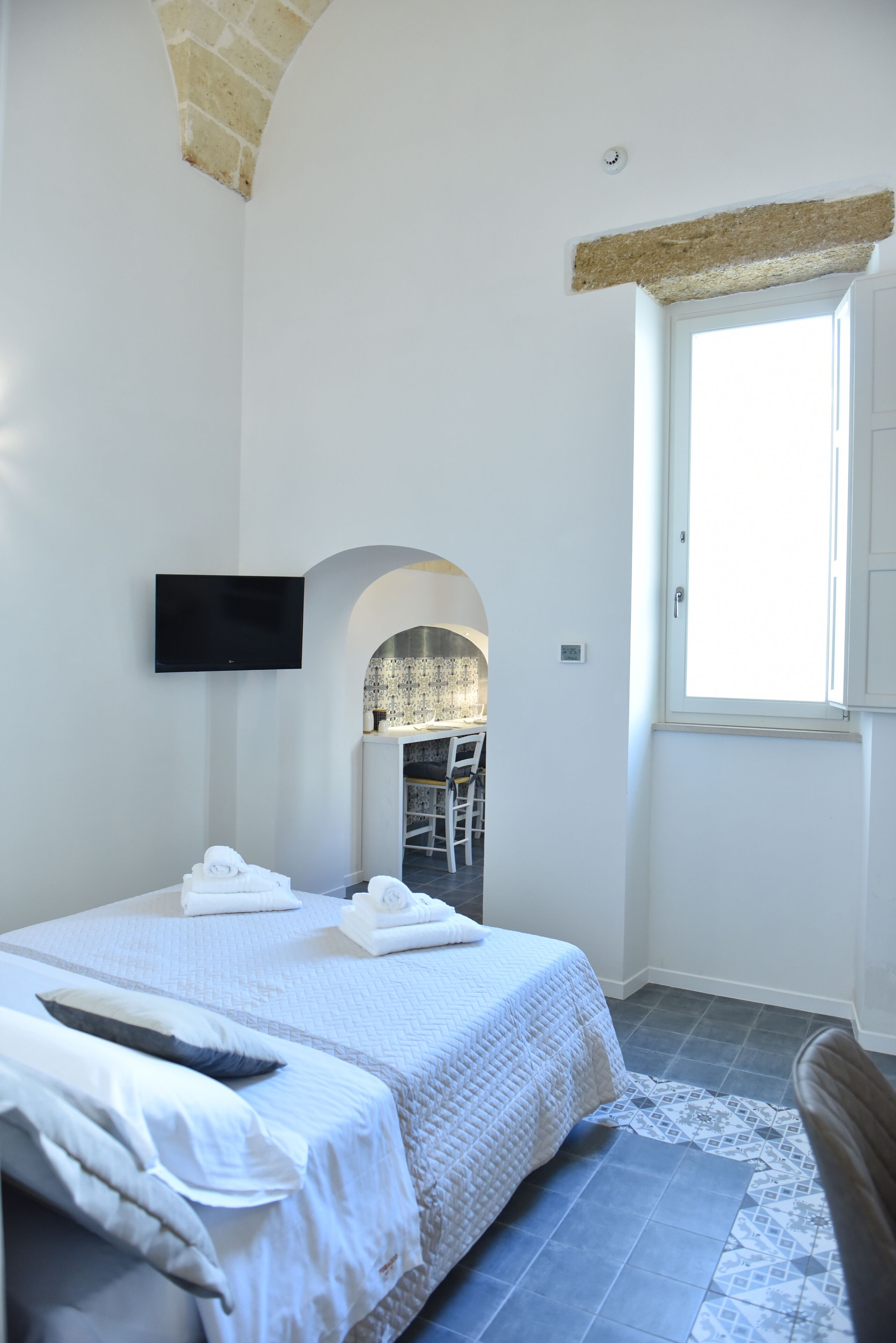 A bedroom with a bed, a TV, a window, and a bathroom visible through an archway.