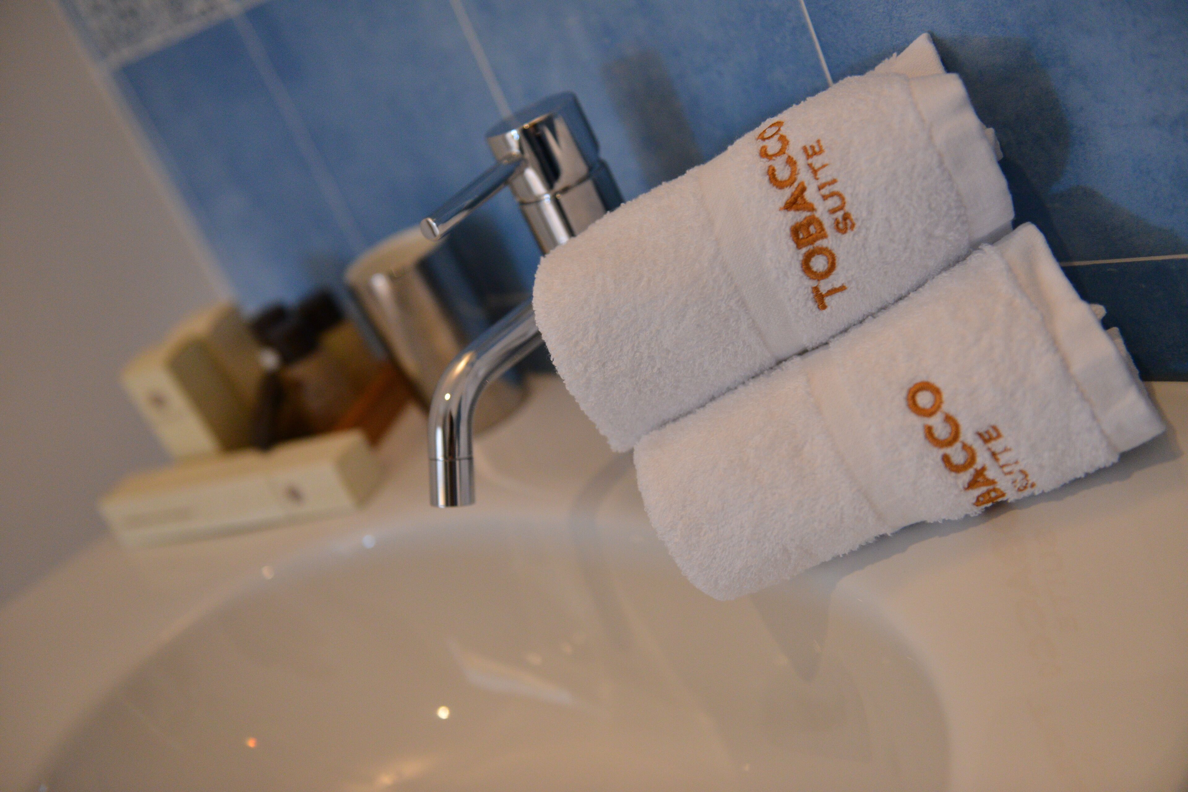 A bathroom sink with two towels labeled "TOBACCO SUITE" hanging on a rack.