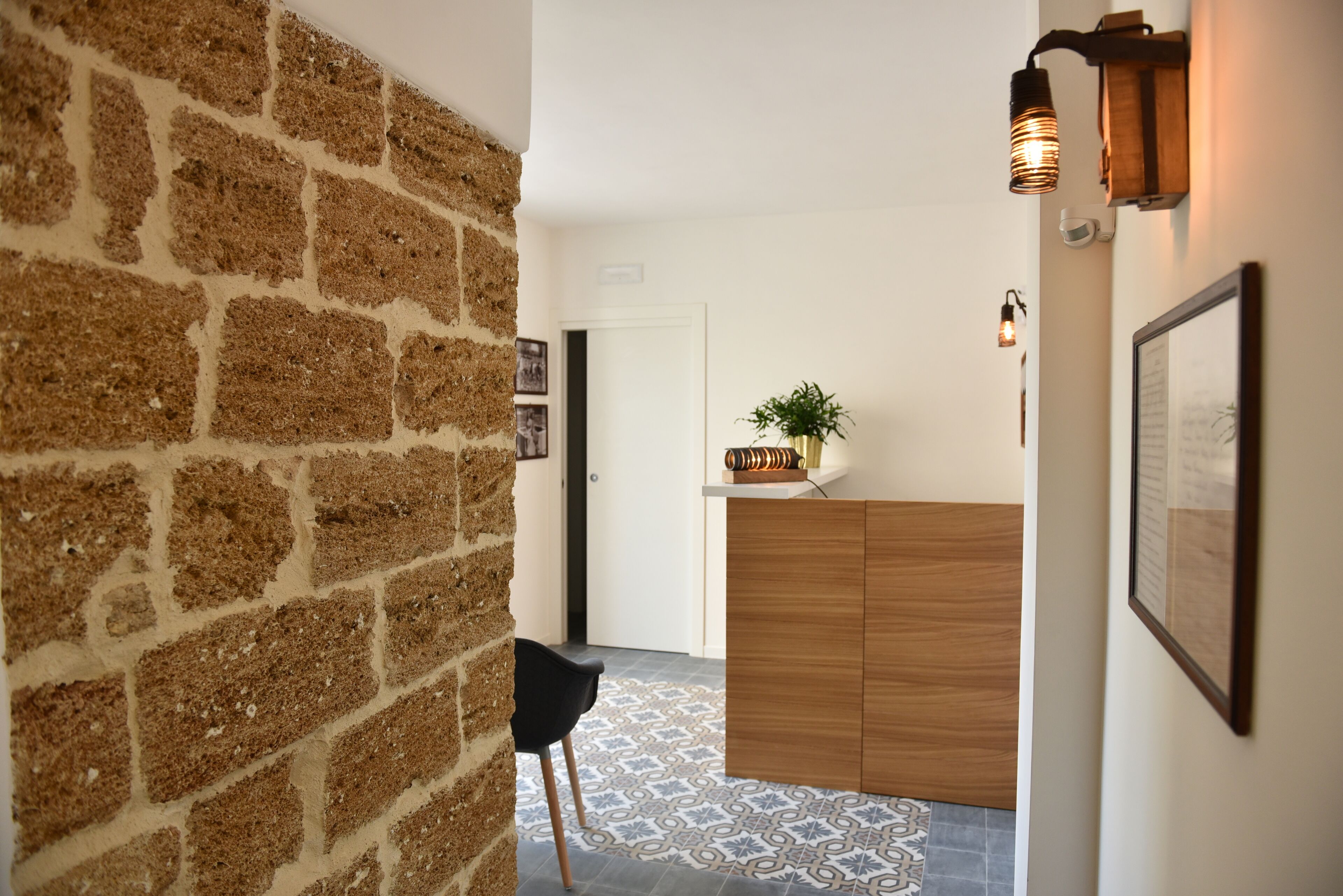 Un pasillo con pared de ladrillo, un mostrador de recepción de madera, una silla negra y baldosas de suelo estampadas.
