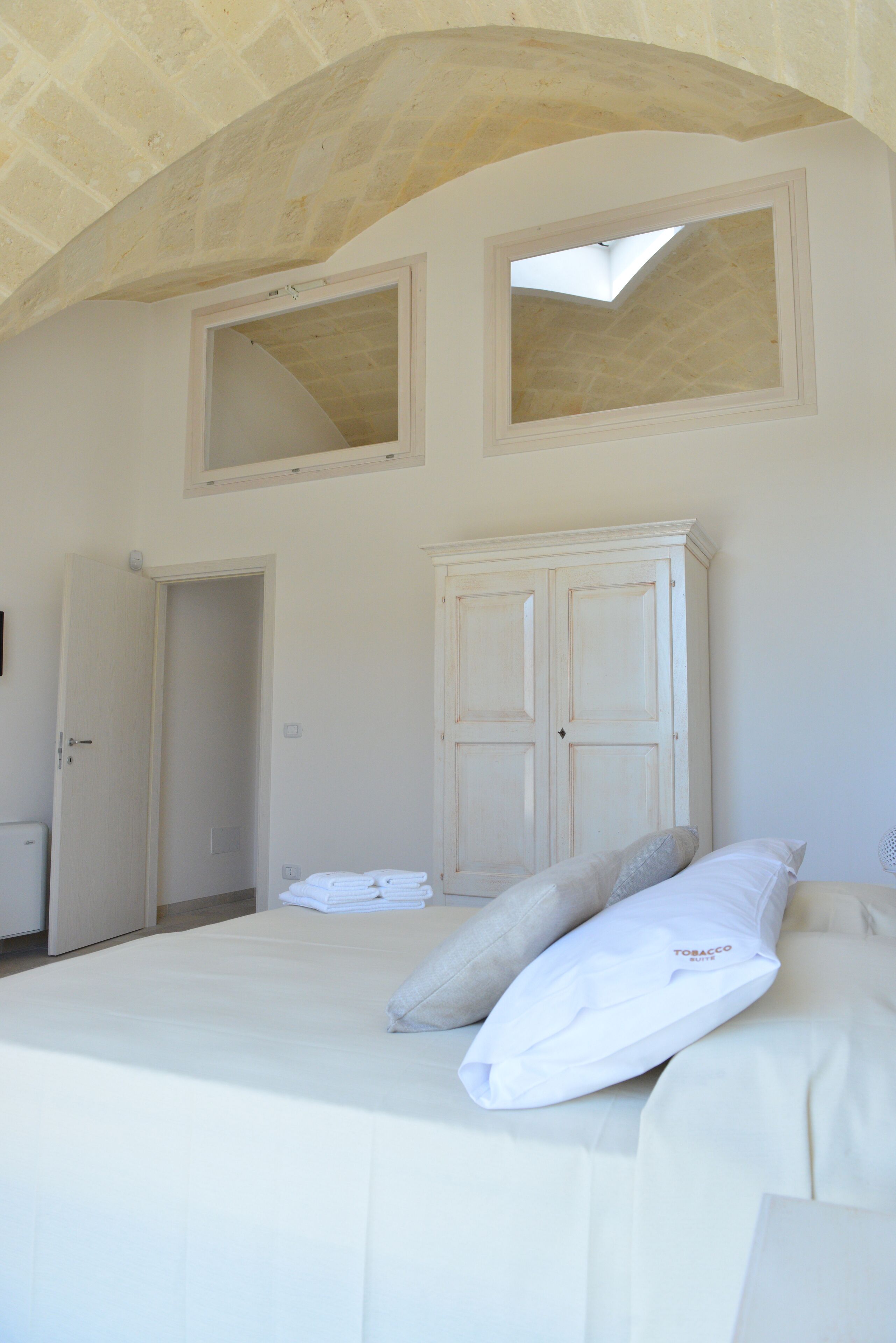 Un dormitorio con cama, armario y dos ventanas.