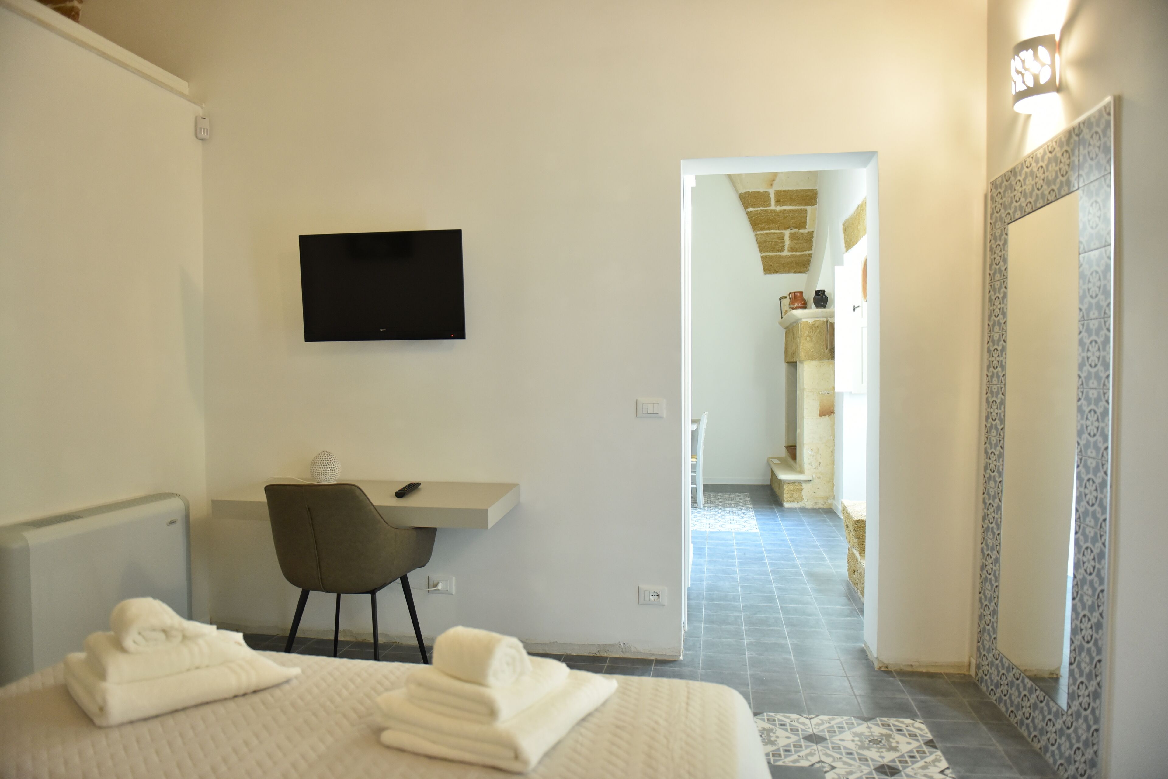 Habitación de hotel con cama, escritorio, silla, televisor y baño visible a través de una puerta abierta.