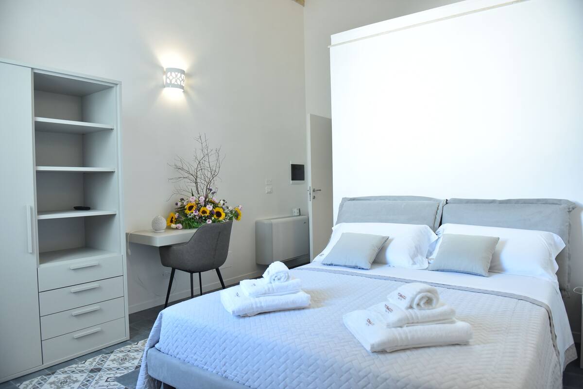 Quarto de hotel com cama, escrivaninha, cadeira e guarda-roupa.
