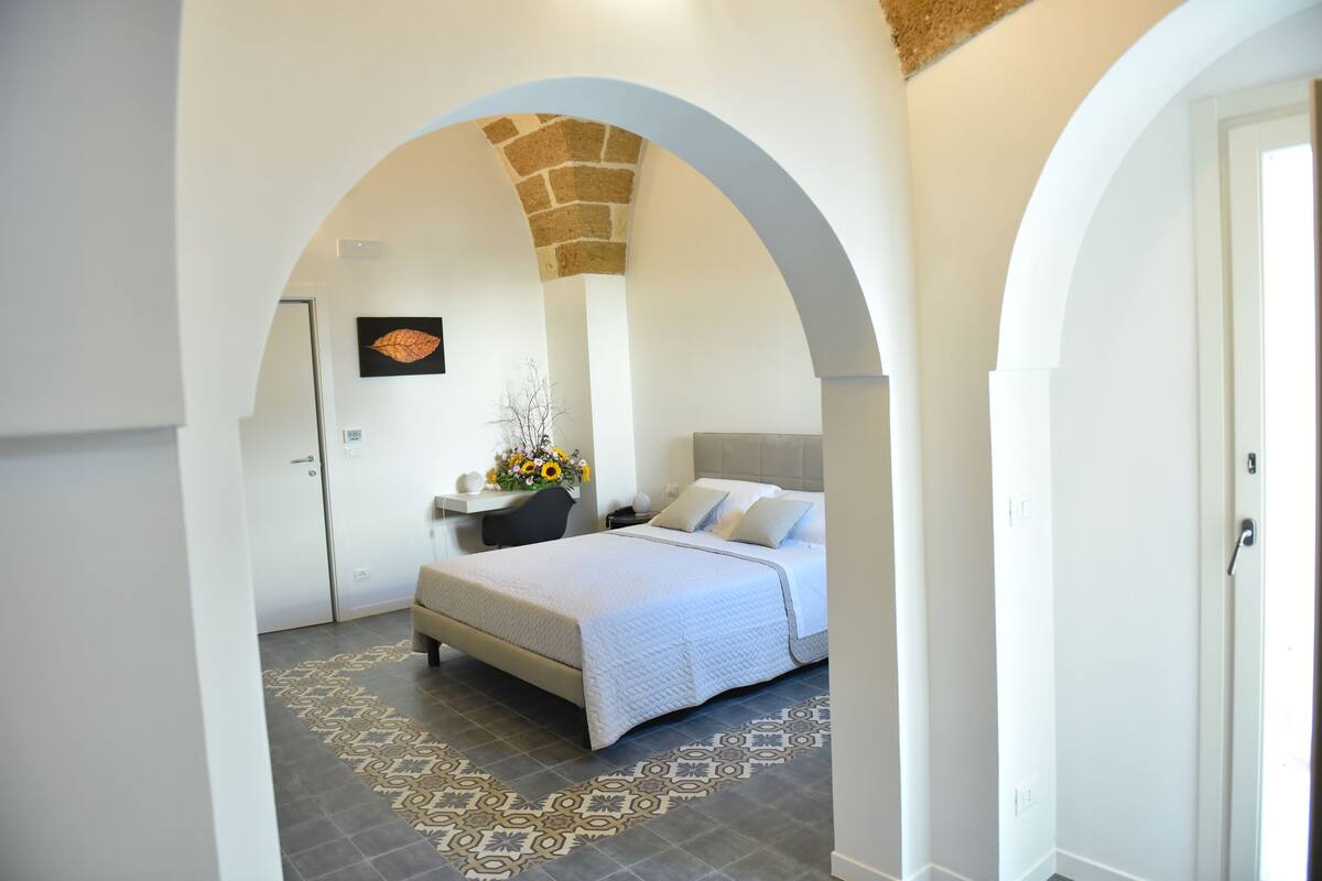 Quarto com cama, mesa de cabeceira e uma obra de arte na parede.