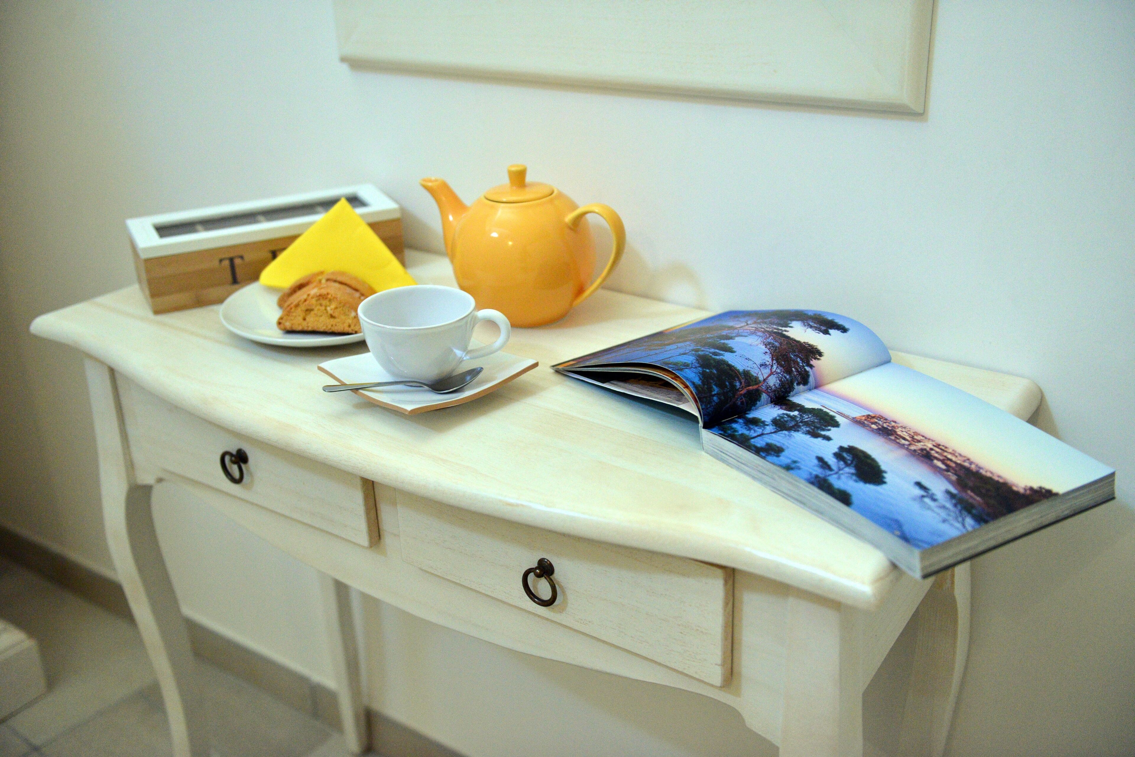 A table with a teapot, a cup, a plate with a pastry, and a magazine.