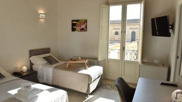 A hotel room with two beds, a desk, a chair, a TV, and a balcony with a view of the city.