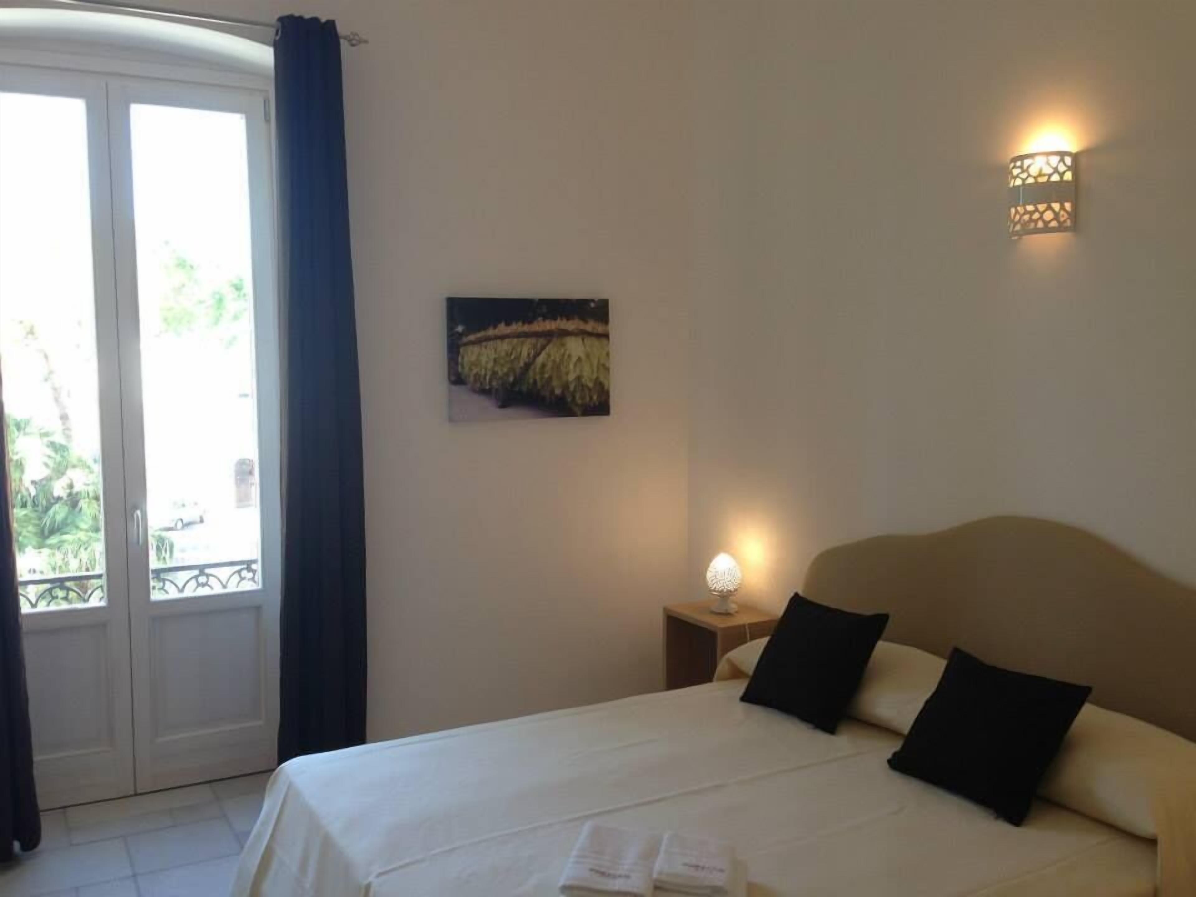 Une chambre d’hôtel avec un lit, une table de chevet, une lampe fixée au mur et un tableau.