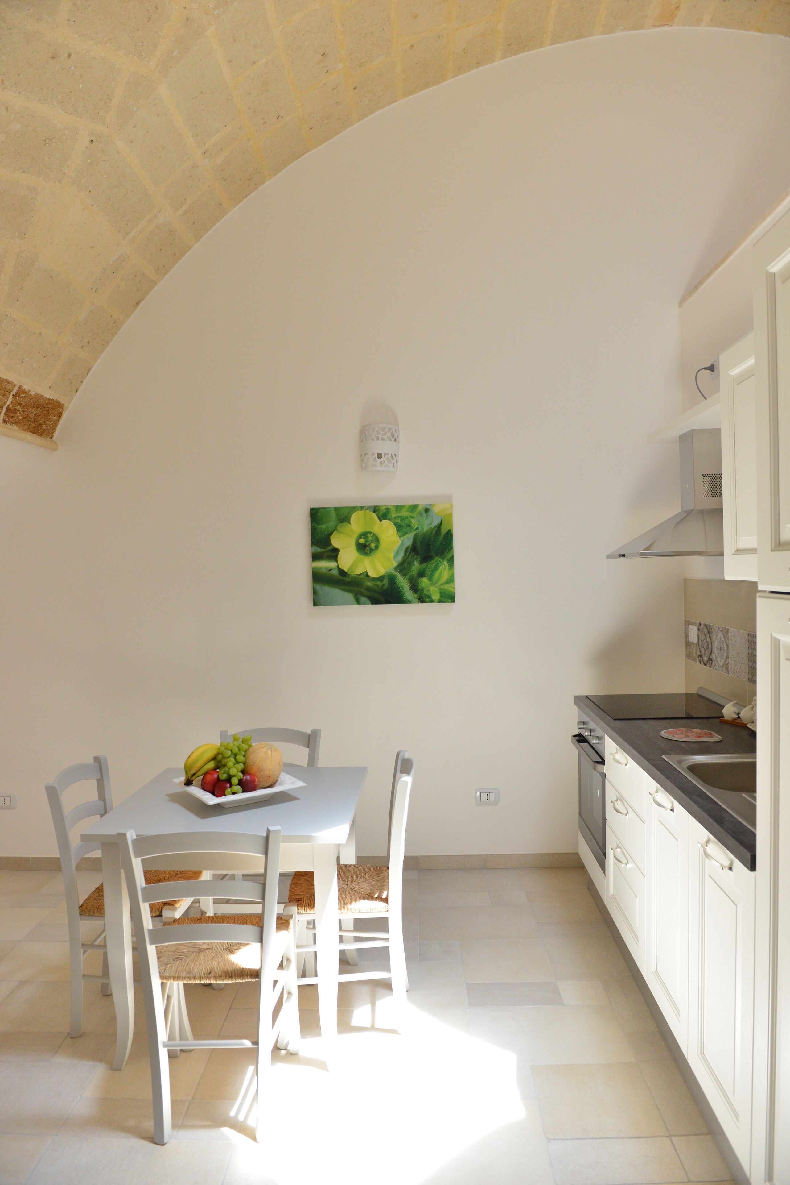 A kitchen with white cabinets, a dining table with chairs, and a fruit bowl.
