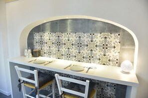 A modern kitchen with a white countertop, two bar stools, and a decorative backsplash. - Tobacco Suite (Mesagne)