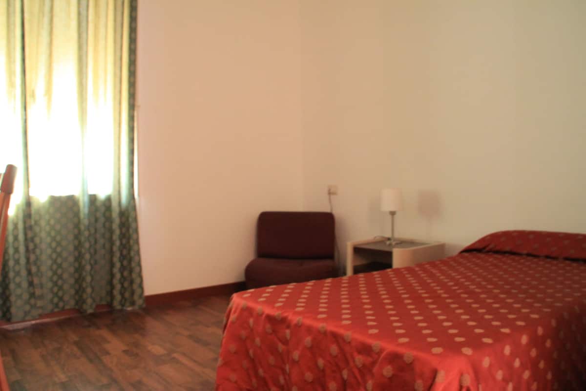 A room with a bed, a chair, a nightstand, and a lamp.
