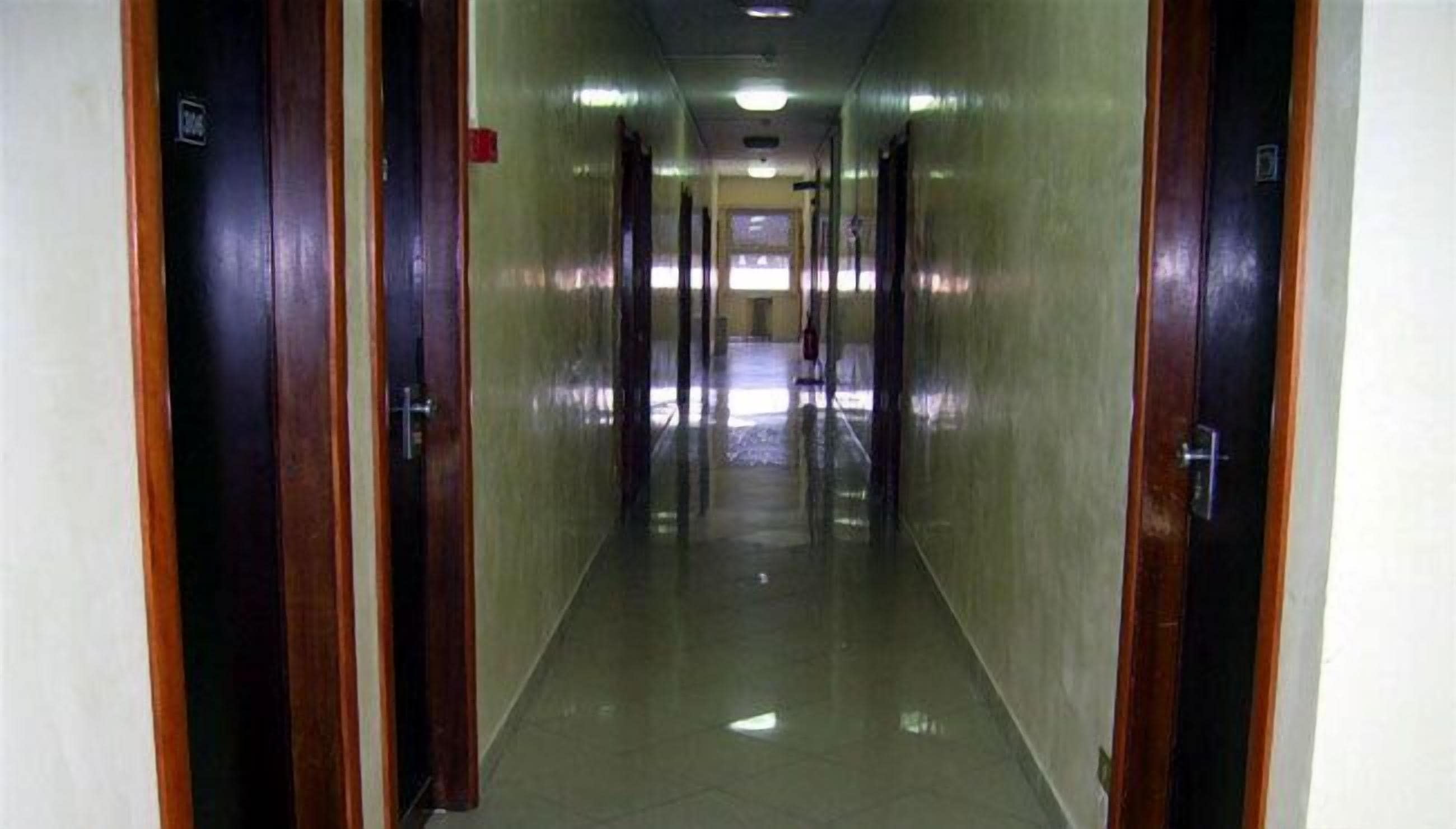 Un pasillo largo y estrecho con puertas de madera a ambos lados, que conduce a una habitación luminosa al final.