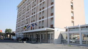 Un hotel de varios pisos con una entrada central, un estacionamiento y varias banderas.