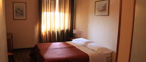 Una habitación de hotel con cama, una silla, un escritorio y una ventana con cortinas.