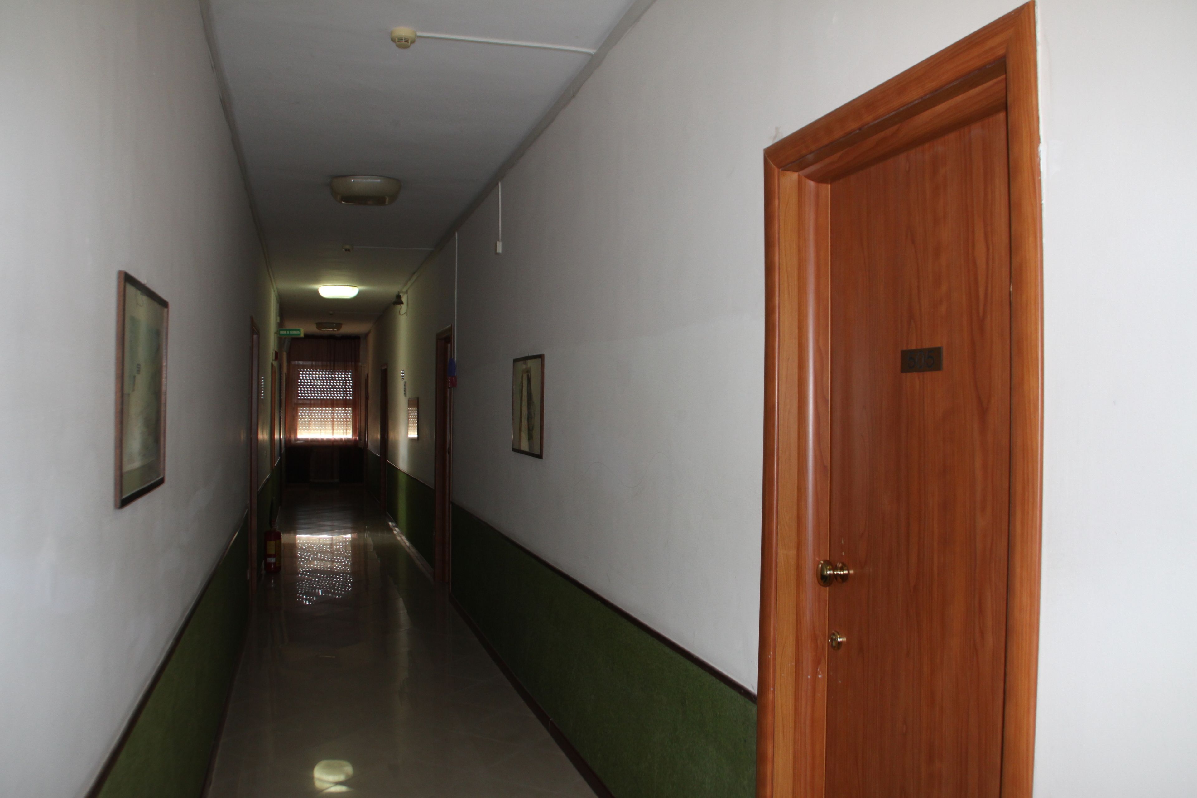 A hallway with a wooden door on the right, green-painted walls, and framed pictures on the left.