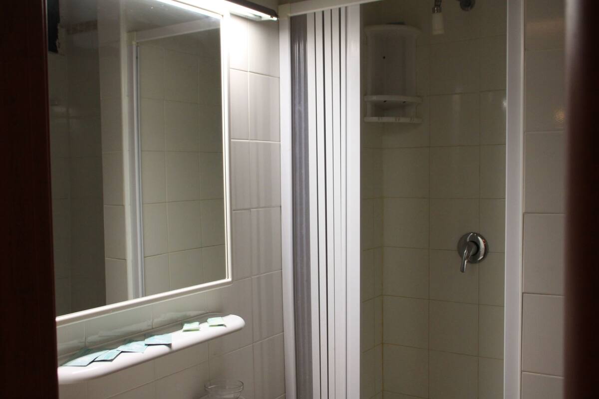 A bathroom with a shower, a mirror, and a shelf with toiletries.