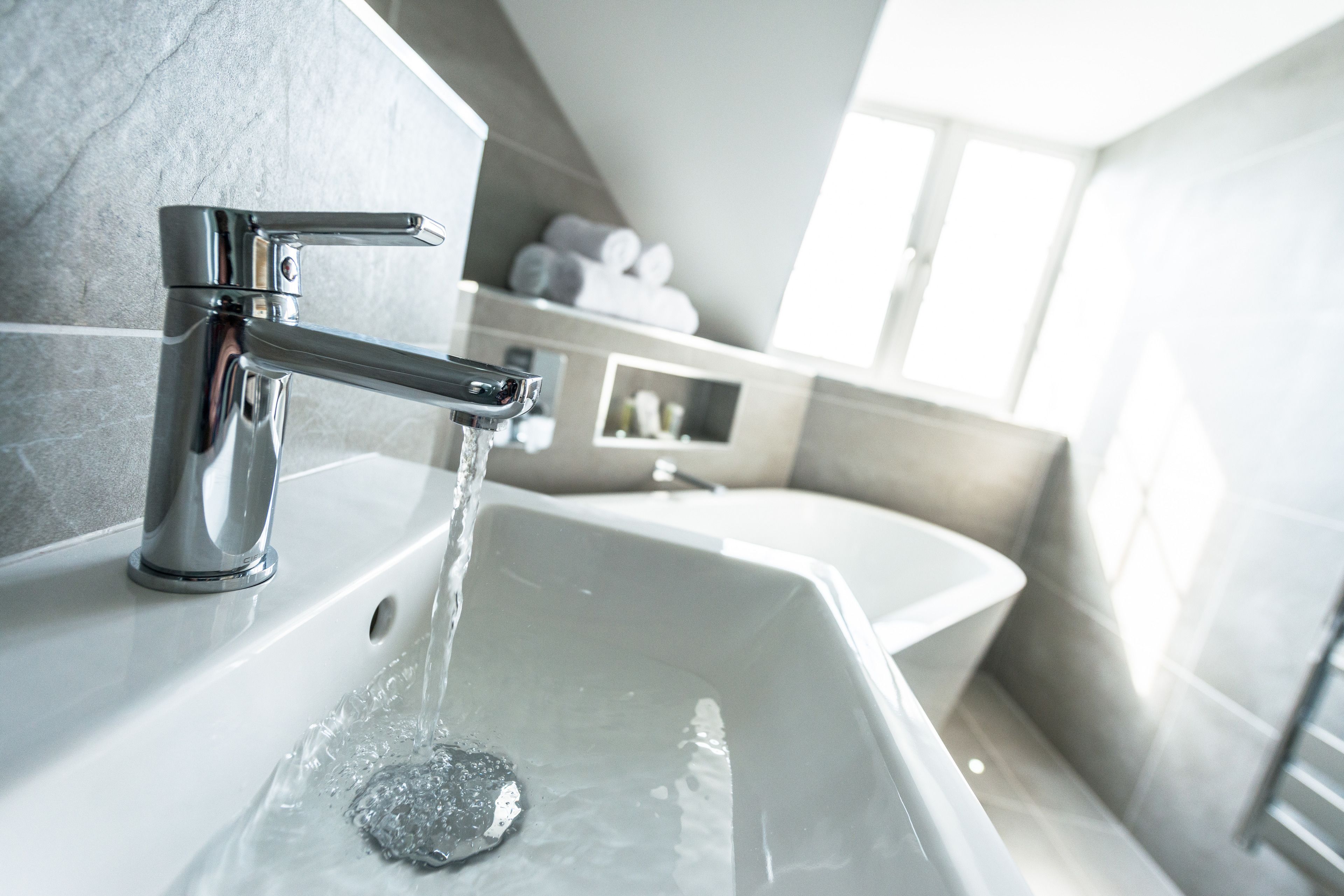 A modern bathroom with a chrome faucet, a white sink, and a towel rack in the background.