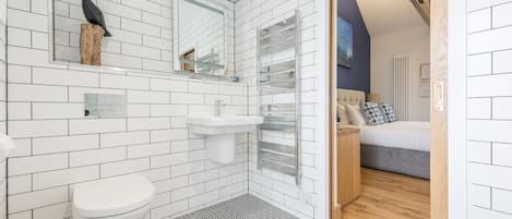 Un baño moderno con azulejos blancos tipo metro, inodoro blanco, lavamanos y zona de ducha.