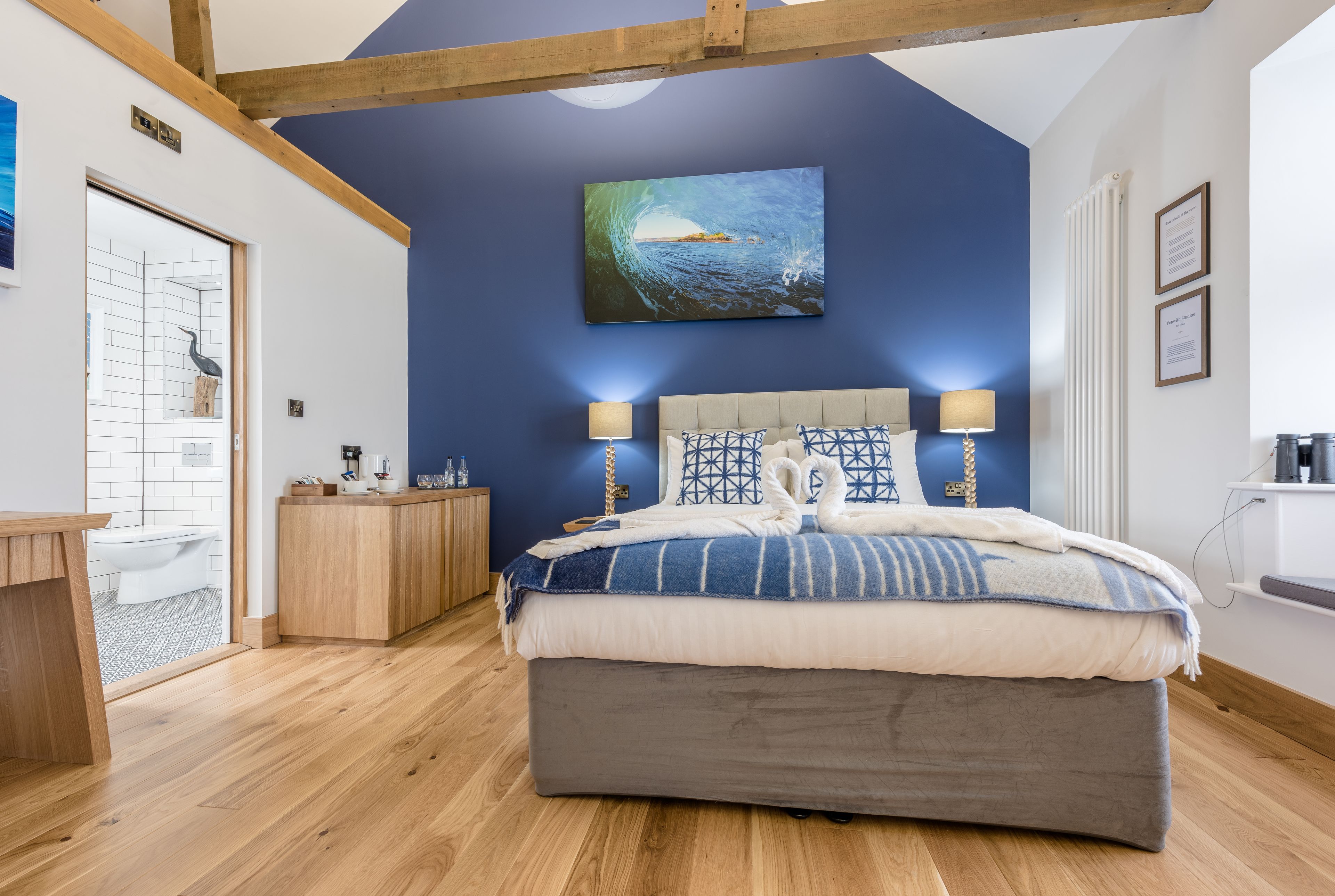 A bedroom with a large bed, wooden headboard, two bedside lamps, a painting of a wave, and a wooden cabinet.