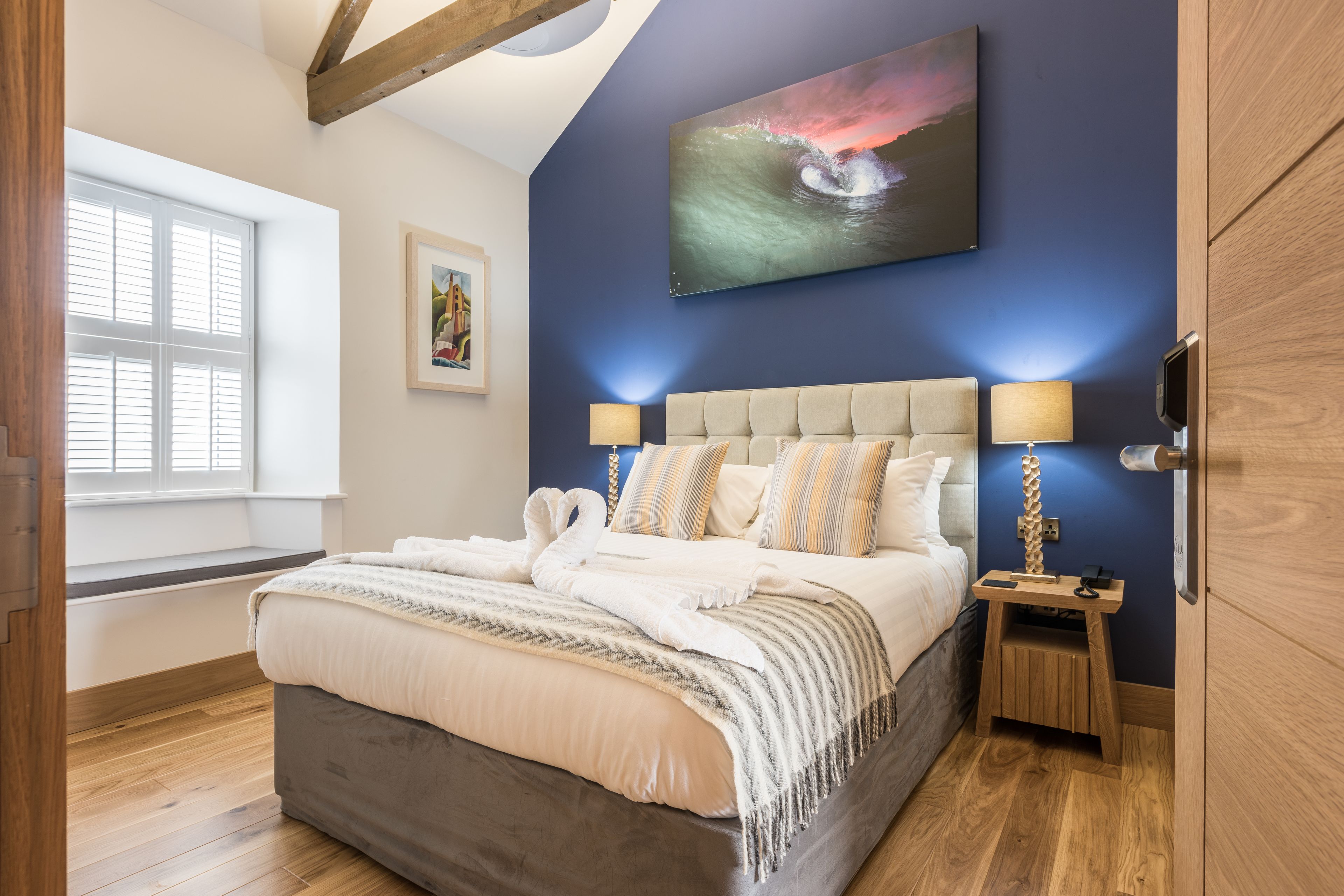 A bedroom with a bed, two bedside tables, a painting, and a window.