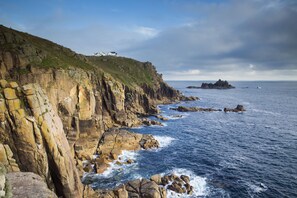 A coastal landscape with rocky cliffs and a small island in the distance. - The Land's End Hotel (Penzance)