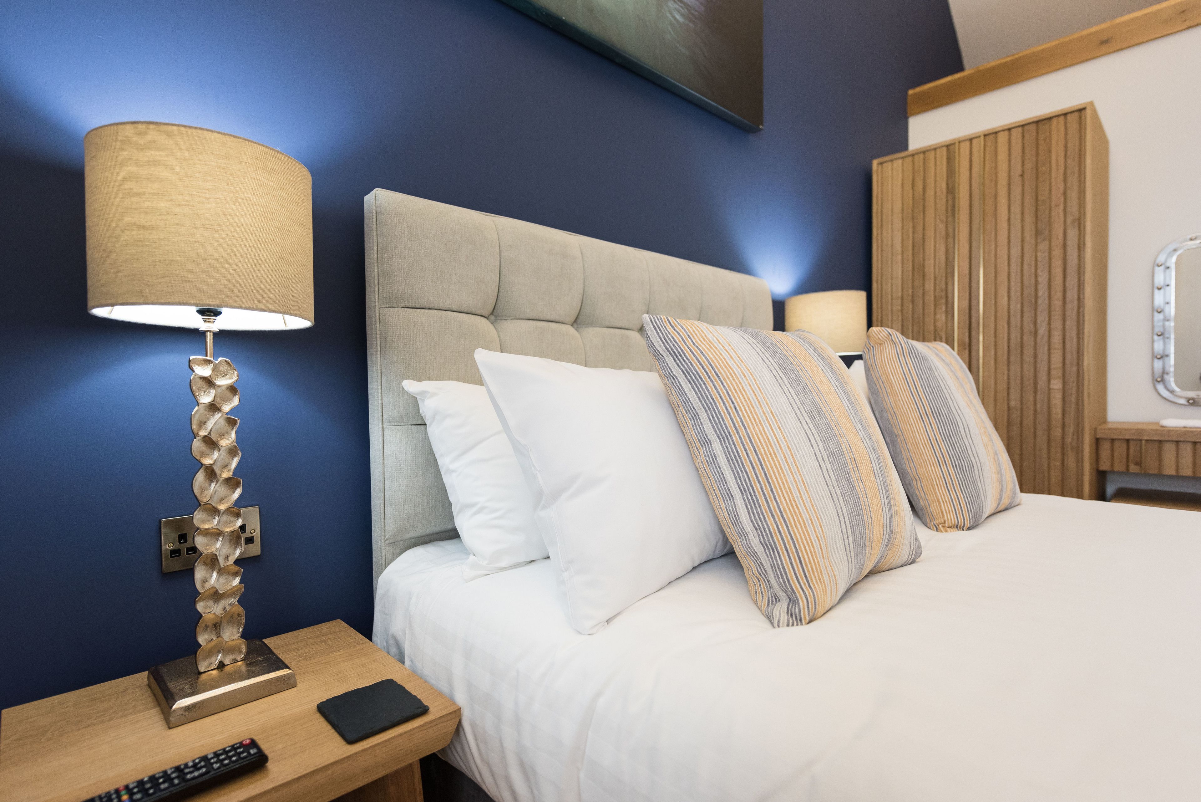 A hotel room with a bed, a nightstand, a lamp, and a remote control.