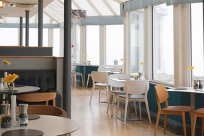 A modern restaurant with high ceilings, large windows, and a mix of seating options including tables and booths. - The Land's End Hotel (Penzance)