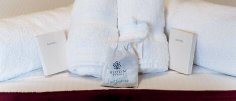 A neatly arranged bed with white towels, two pillows, and a small bag with the text "BLOOM remedies Sweet Dreams".