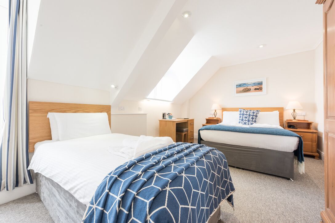 A bedroom with two beds, a wooden headboard, bedside tables, and a painting on the wall.