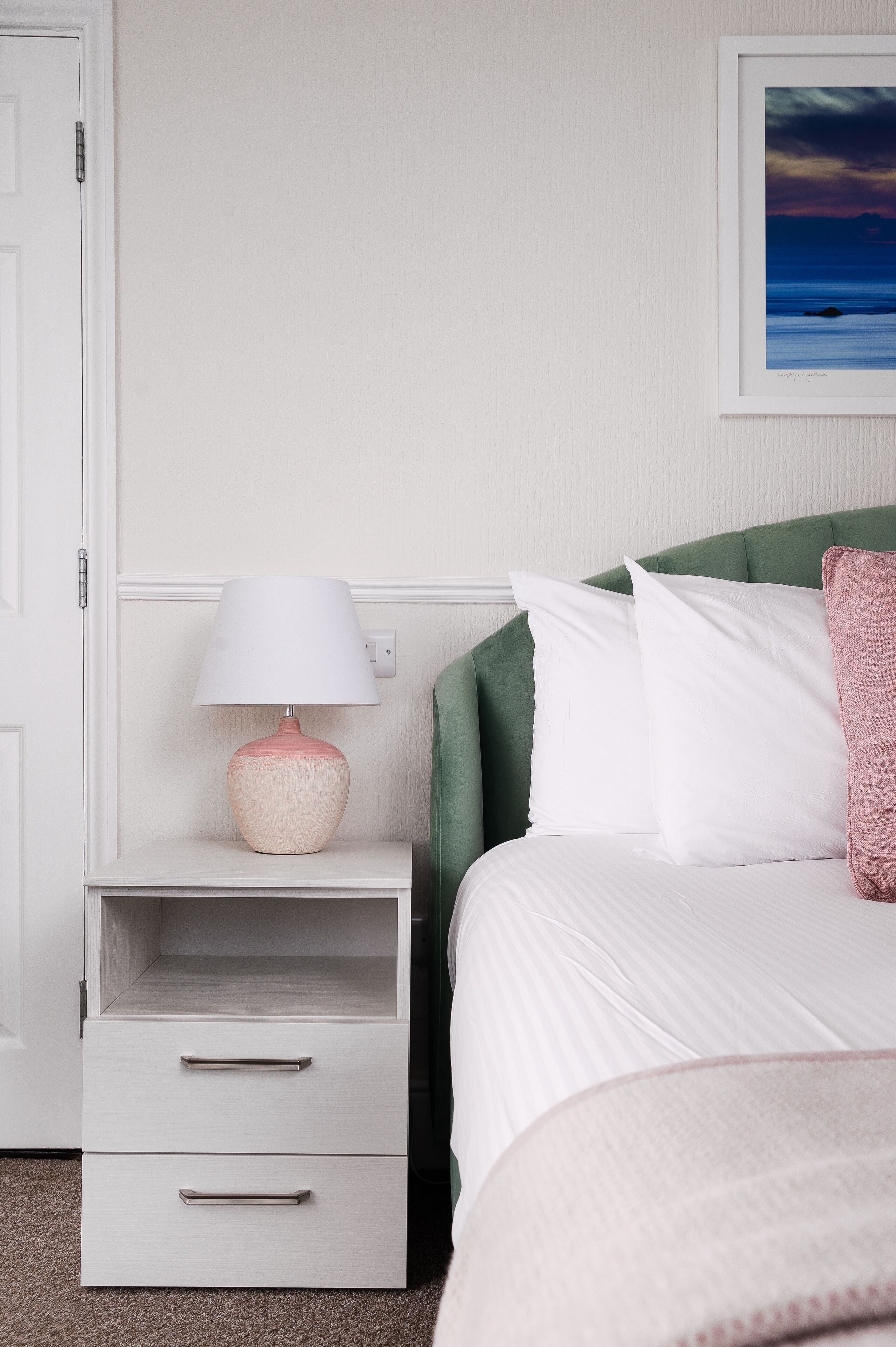 Een keurig opgemaakt slaapkamer met een bed, een nachtkastje met lamp en een ladekast.