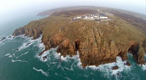 An aerial view of a coastal property with a large house surrounded by cliffs, a small boat docked near the shore, and a rugged coastline. - The Land's End Hotel (Penzance)