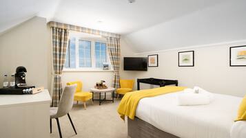 A hotel room with a bed, a desk with a coffee maker, a chair, a small table, and a TV on the wall.