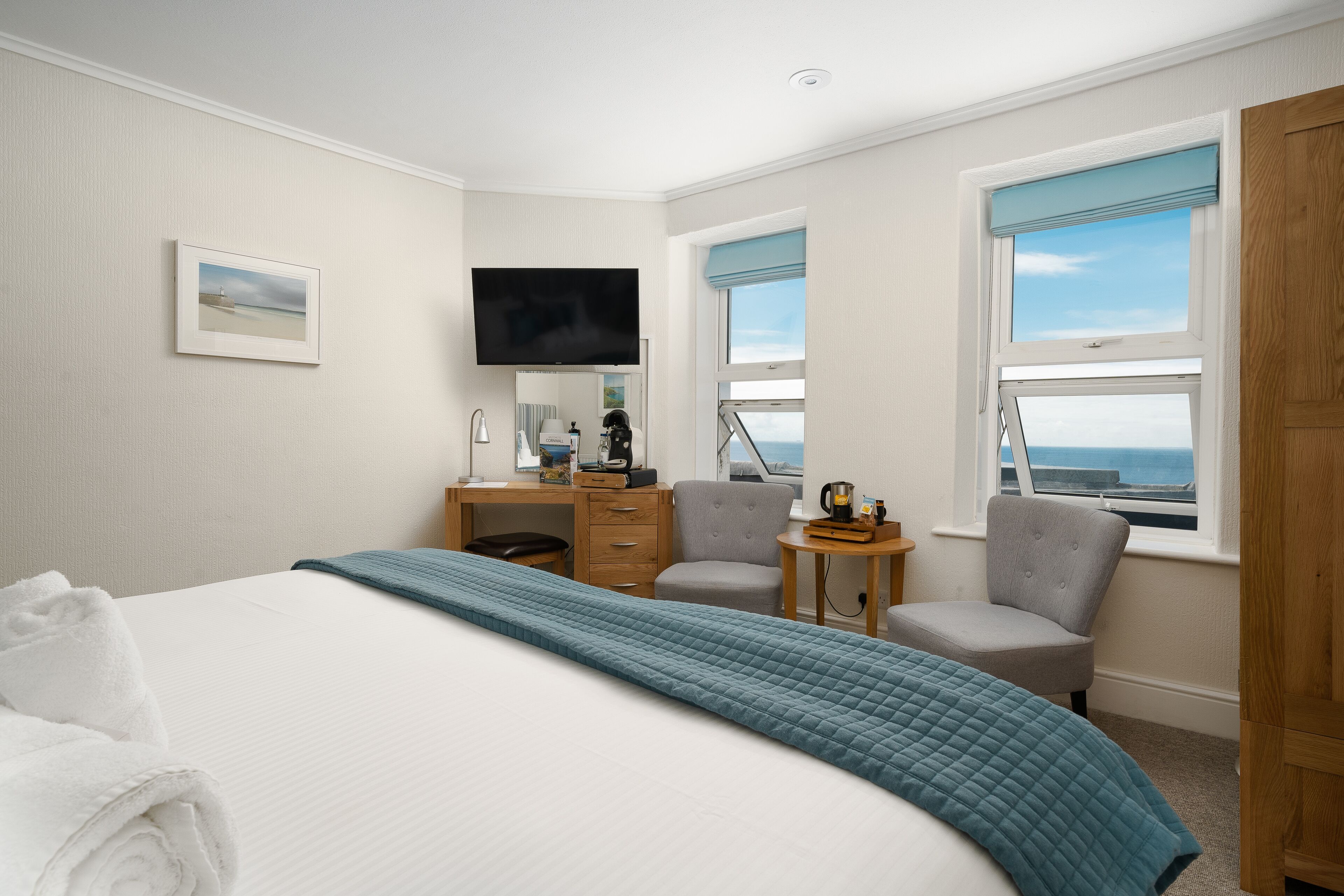 A hotel room with a bed, a desk, a chair, a television, and a window with a view of the sea.