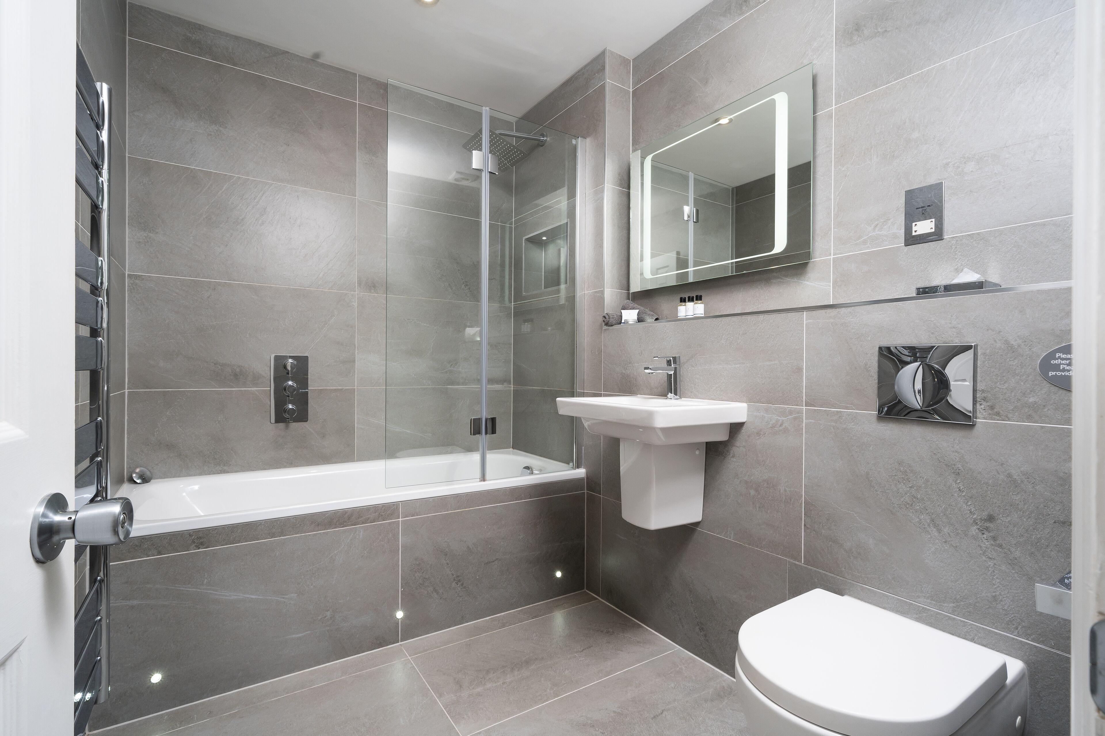A modern bathroom with a glass-enclosed shower, a white bathtub, a sink, and a toilet.