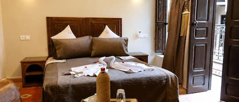 A neatly made bed with pillows, a bedside table with a bottle and glass, a chair, and a colorful rug.