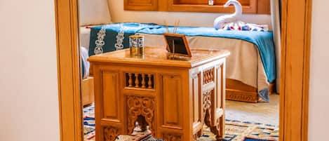 Una habitación con una cama, una mesita de madera con una computadora portátil, un cisne decorativo y una alfombra estampada.