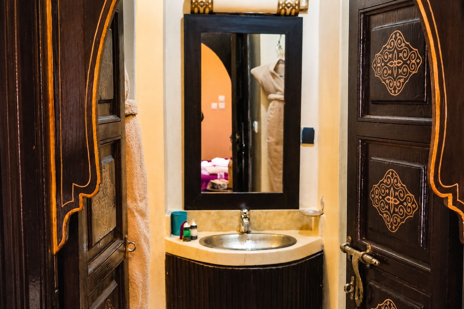 A bathroom with a sink, mirror, and ornate wooden doors.