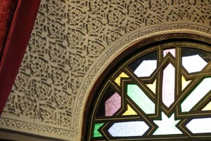 Una ventana de vitral con diseños geométricos y un techo decorativo con detalles elaborados.