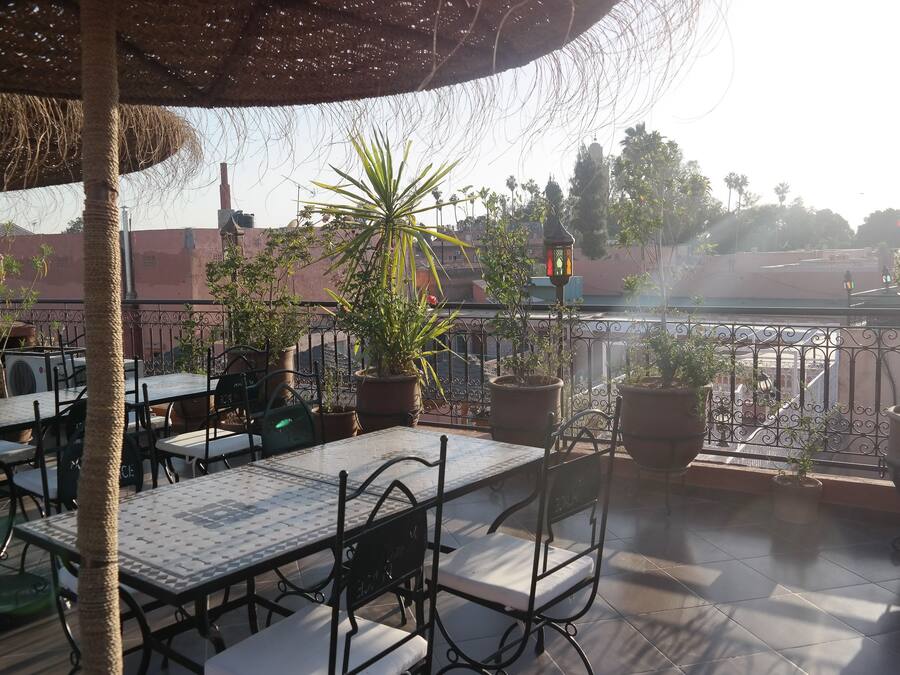 Un patio al aire libre con mesas y sillas, plantas en macetas y vistas de edificios al fondo.