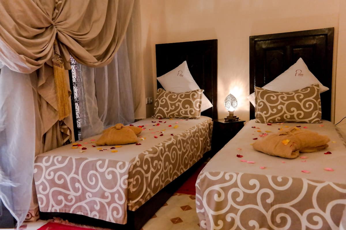 Two twin beds with patterned bedding, a decorative curtain, and a bedside table with a lamp.
