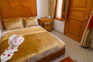 Un letto ben rifatto con asciugamani e decorazioni a forma di cuore, un comodino in legno, una porta in legno e piastrelle a motivi.