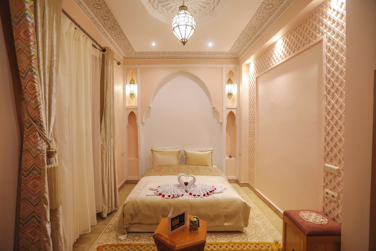 A hotel room with a large bed, decorative pillows, a small table with a remote control, and a decorative wall panel.