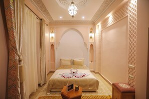 A hotel room with a large bed, decorative pillows, a small table with a remote control, and a decorative wall panel.