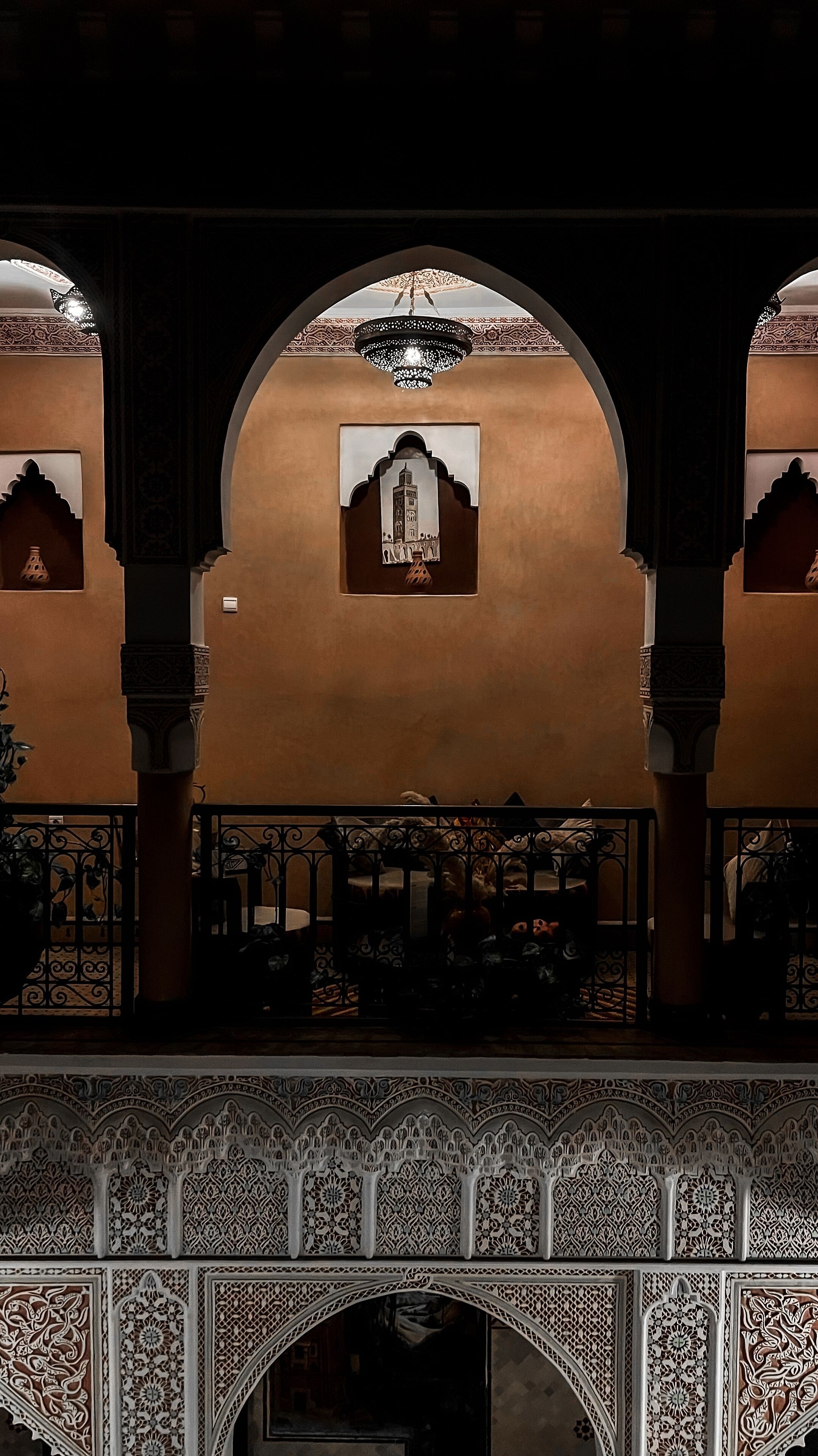 An interior view of a building with arches, a chandelier, and intricate wall designs.