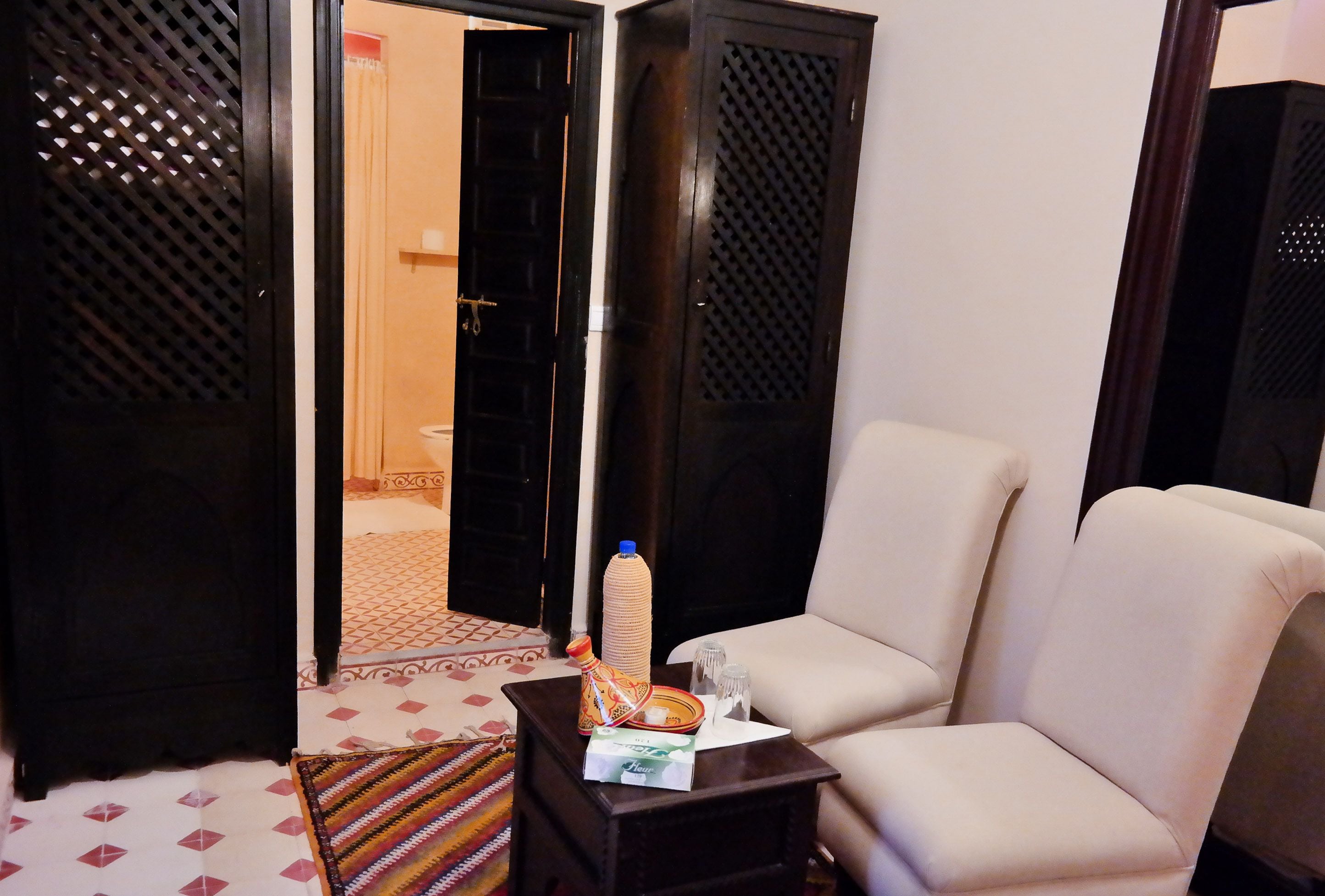 A living room with a sofa, a small table with a bottle and a tissue box, and a patterned rug.