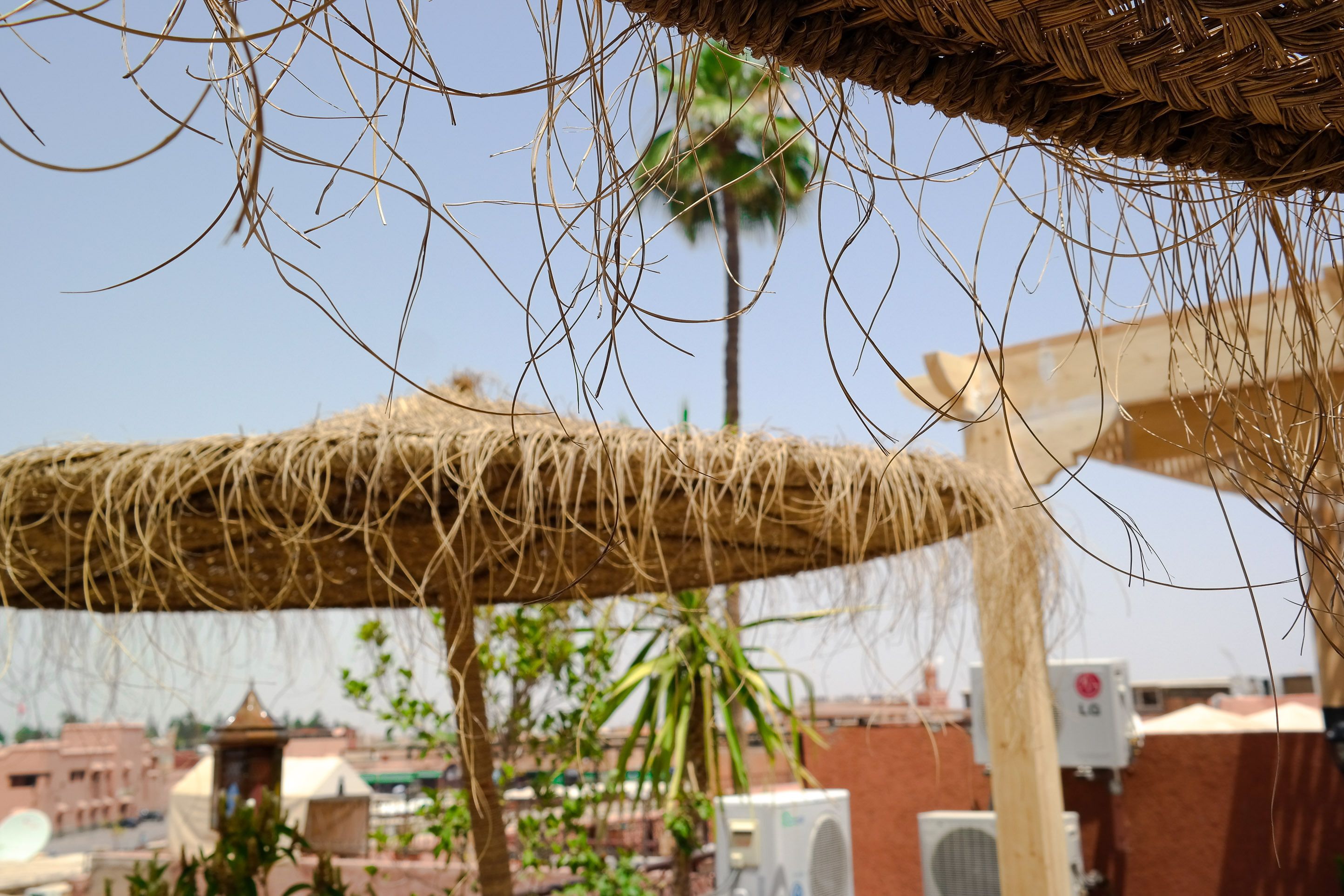 A thatched roof structure with a view of buildings and palm trees in the background.