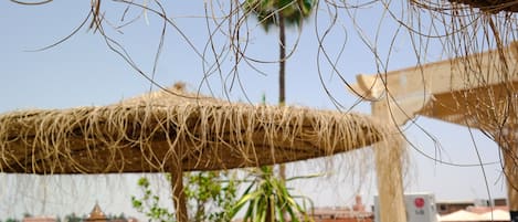 A thatched roof structure with a view of buildings and palm trees in the background.