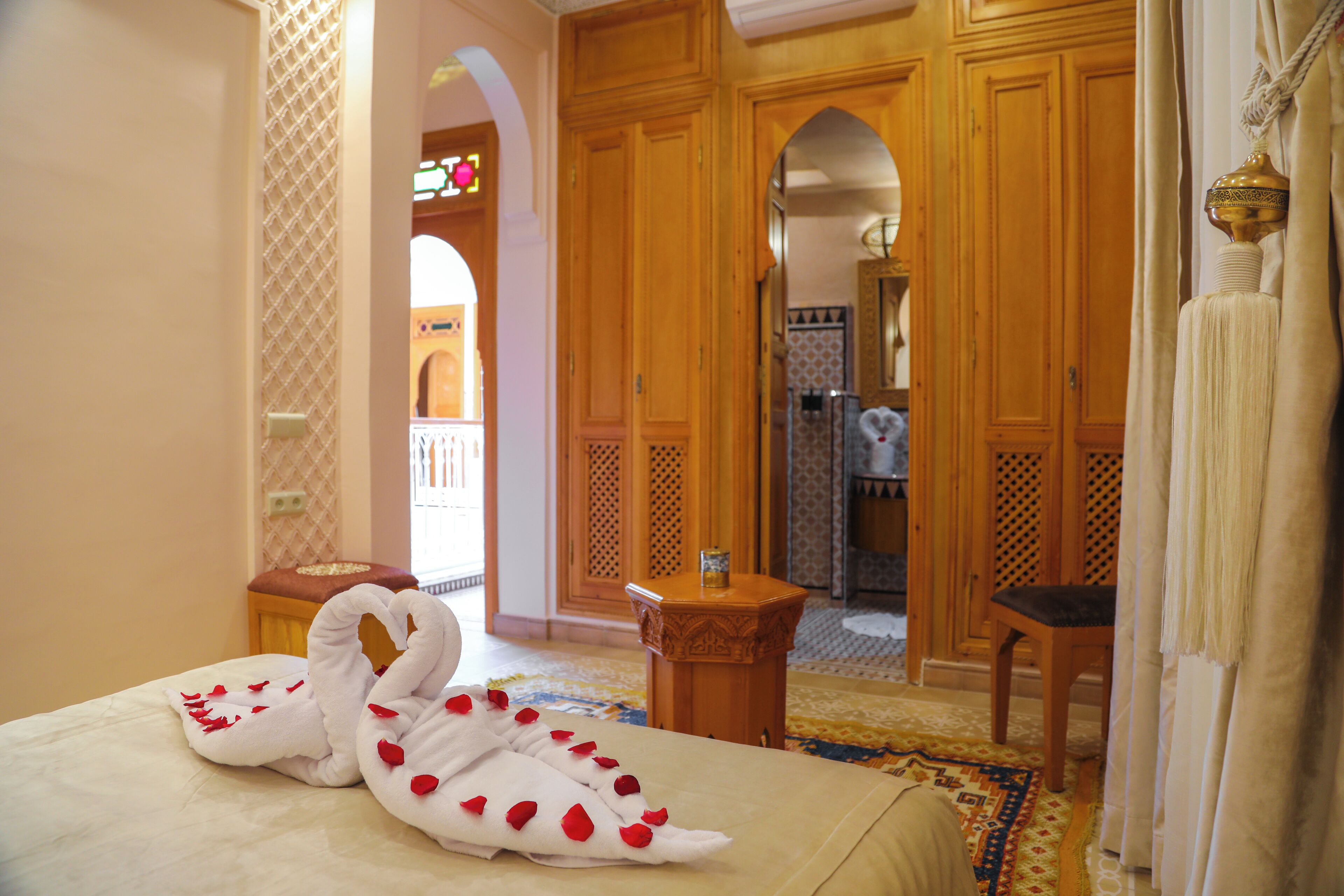 A hotel room with a bed, a wooden wardrobe, a small wooden table, and a chair.
